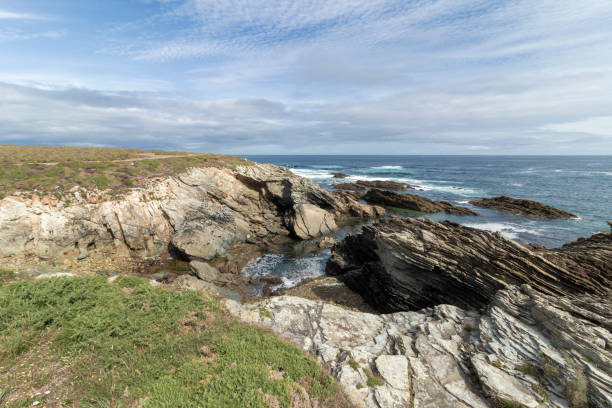 istock A rocky coastline with greenery, under a partly cloudy sky, waves crashing against the rocks, creating a serene atmosphere 2071836493