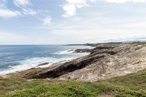 rocky coastline with greenery, overlooking a vast, serene ocean under a partly cloudy sky.