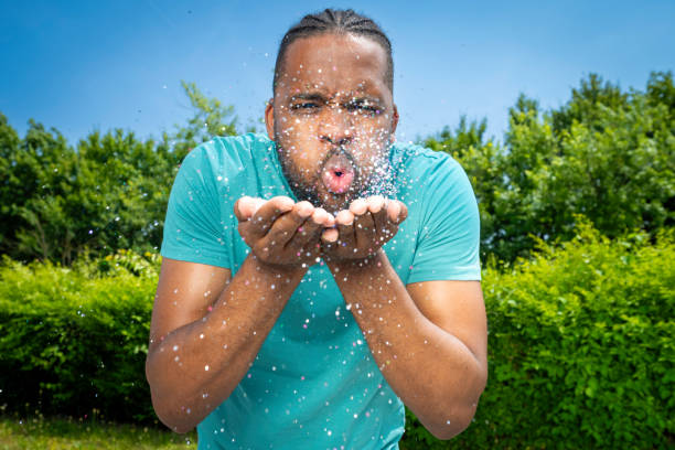 A young Caucasian man wearing a black t-shirt and glasses stares straight ahead from a side angle as his body disperses into a bunch of tiny particles floating around him sucked to the sky above him.