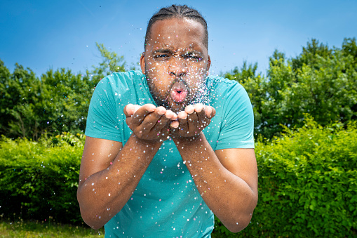 Young african american man blowing glitter from hands at camera portrait outdoors
