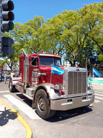 Buenos Aires, Argentina - Nov 6, 2022: Red Peterbilt 379 heavy duty cargo truck in a treelined street at a classic car show in a sunny day. Copyspace