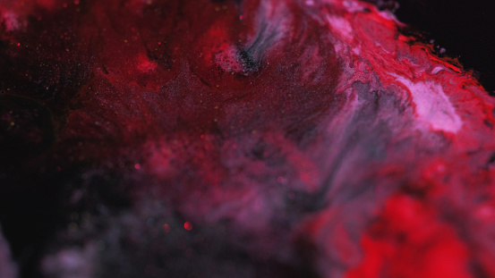 Ink spill. Paint splatter. Blur red silver black color shimmering particles texture acrylic fluid blotch mix spreading motion abstract art background.