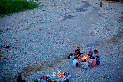 Yangyang County, South Korea - July 30, 2019: A group of locals gathered on the rocky beach near Mulchi Port, forming a circle around a small fire for a picnic, with a blanket laid out nearby after sunset.