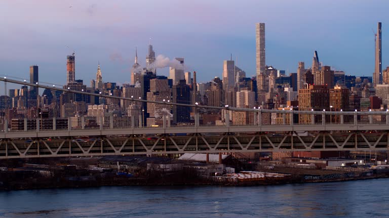 Manhattan Midtown and East Side Skyline, with Chrysler Building, Empire State Building, and other skyscrapers illuminated with city lights behind the Robert F. Kennedy Bridge. Drone footage with the panning camera motion.