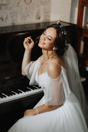Portrait of a beautiful girl in a wedding dress and a wreath of fresh flowers on her head, playing the piano, playing alone