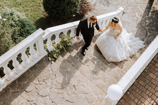 portrait of a young beautiful wedding couple in the garden, the bride in an off-the-shoulder wedding dress circling and showing off her dress, the groom in a black classic suit