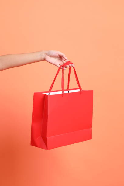 HAPPY SONGKRAN DAY. Cheerful lovely young asian woman in summer clothing with gesture of holding shopping bag isolated on orange background. Songkran festival. Thai New Year's Day.