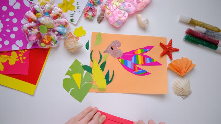 Child making homemade greeting card, applique with bird, hummingbird or colibri and flowers from pieces of paper, tropical garden. Gift for Mothers day, Birthday, Easter, holidays.