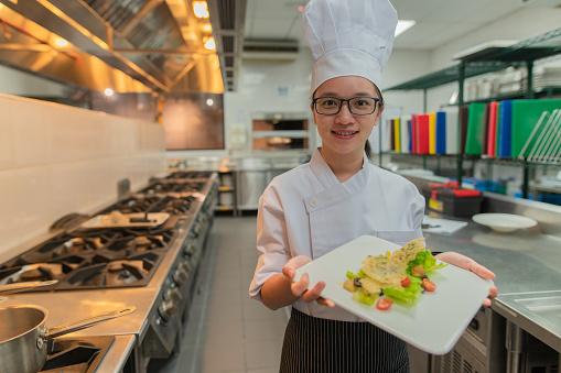 Asian female kitchen apprentice decorate the food before serve to customer