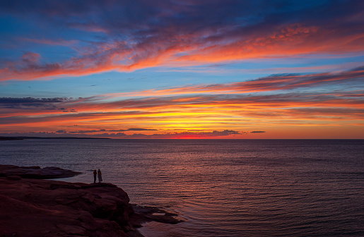 Young couple enjoying a colorful sunset on the Gulf of St Lawrence coast. Dramatic sky in red and orange shades. Oceanview Lookoff, PEI National Park.