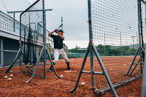 From a rear perspective, the baseball batter is practicing hitting skills and swinging the bat to hit the baseball.