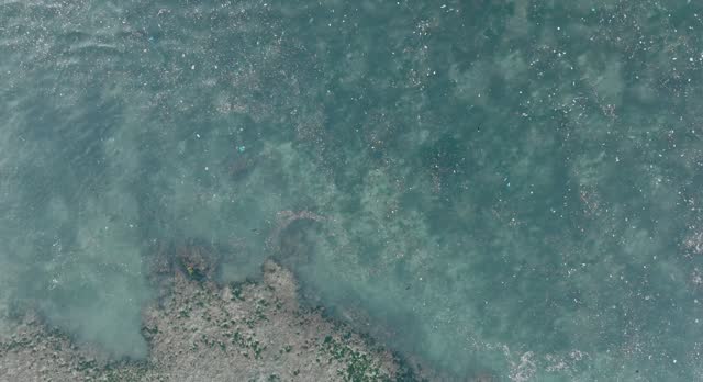 Top down drone shot of polluted water filled with plastic trash and dead coral reef in the turqouise tropical water of Balangan Beach Uluwatu Bali Indonesia