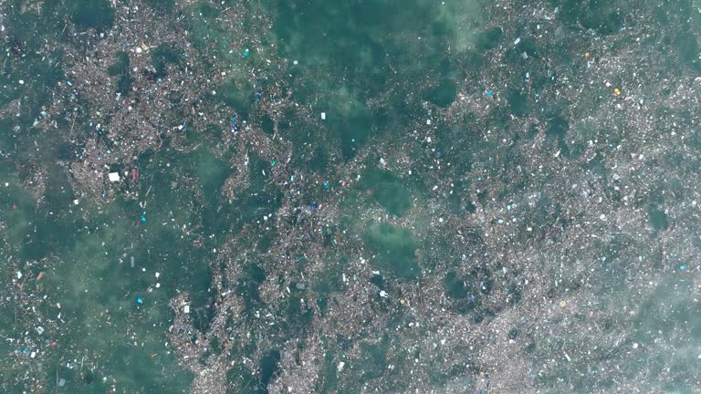 Low altitude top down ascending drone shot of polluted water filled with trash floating over dead coral reef in the turqouise tropical water of  Bali Indonesia