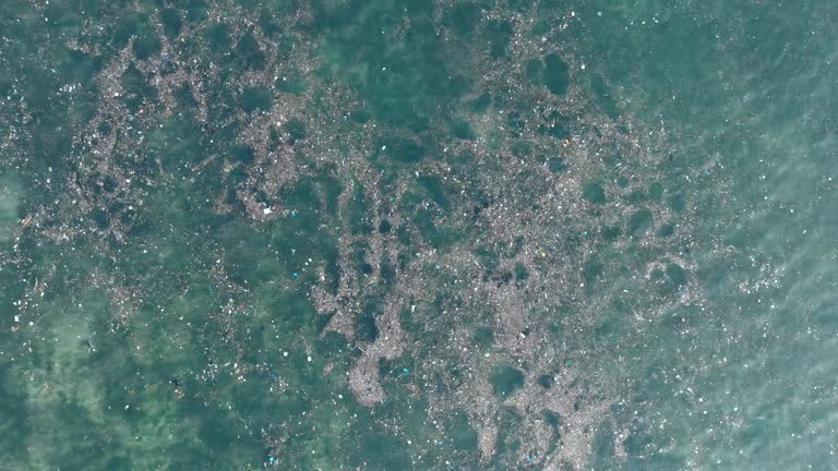 High altitude top down ascending drone shot of polluted water filled with trash floating over dead coral reef in the turqouise tropical water of  Bali Indonesia