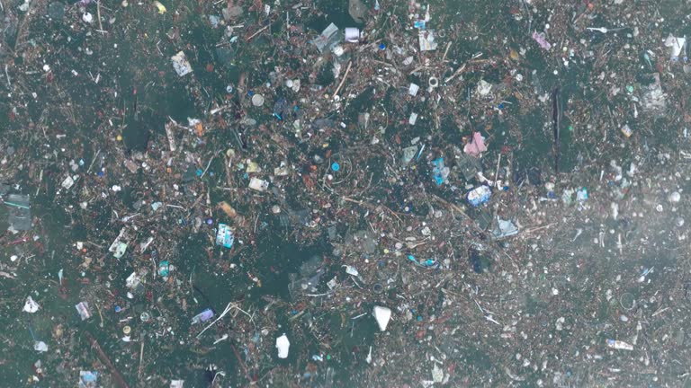 Low altitude top down drone shot of polluted water filled with trash floating over dead coral reef in the turqouise tropical water of  Bali Indonesia