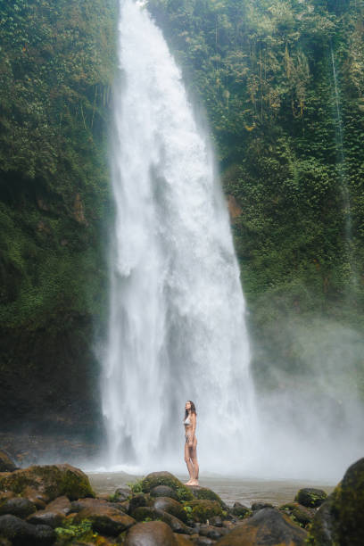 istock Woman standing near the refreshing powerful  waterfall on Bali 2072491579