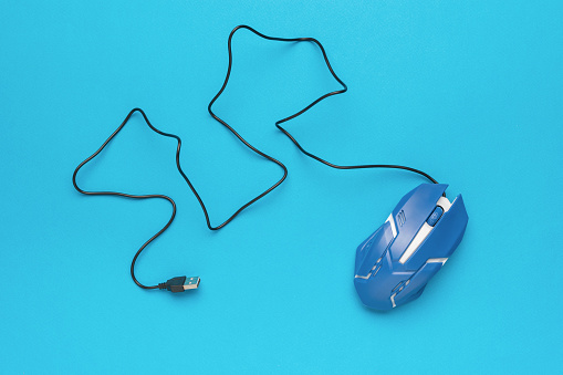 A blue computer mouse with a USB cable on a blue background. An accessory for a personal computer.