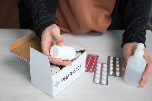 Woman at home taking medications out of box, online pharmacy delivery, health care