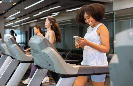 Young African American woman exercising on  treadmill at a gym.Woman Chat and texting mobile on treadmill. smile and funny emotion.