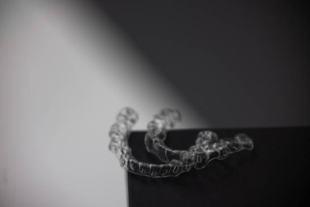Invisible orthodontics cosmetic brackets on gradient background, tooth aligners, plastic braces. Invisible orthodontics cosmetic brackets on gradient background, tooth aligners, plastic braces. Modern teeth retainers created on a 3d printer. A way to have a beautiful smile and white teeth. High quality photo chemical straightener stock pictures, royalty-free photos & images