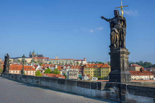 Statue of St. John the Baptist on Charles Bridge, with Hradcany castle and St. Vitus Cathedral in the background, in Prague, Czech Republic, in sunny day