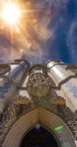 Statue or sculpture of Triton, Greek god of the sea, on a shell with decorative stone carving that guards the entrance to the Pena Palace, under a spectacular sky with sparkles and rays of the sun.