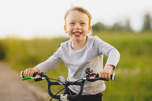 happy young boy three years old child on his new bicycle outdoors in meadow smiling at camera, medium shot portrait shallow focus