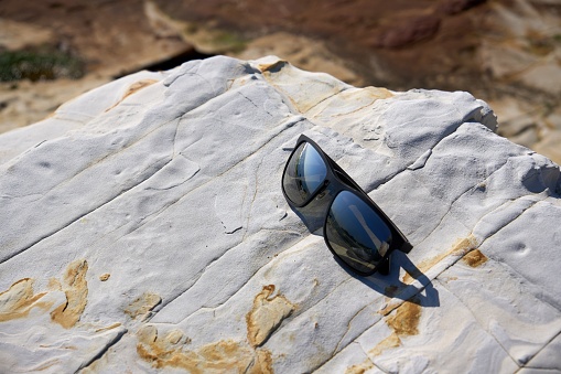[Minamichita] Sunglasses placed on a rocky area on the coast.
