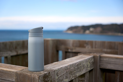 Gray water bottle placed on a wooden pillar with the sea in the background.