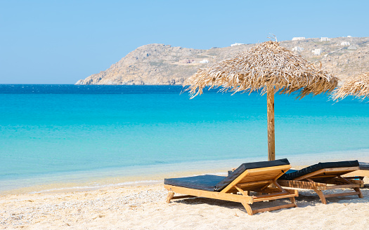 Mykonos beach during summer with umbrella and luxury beach chairs beds, blue ocean with the mountain at Elia beach Mikonos Greece.