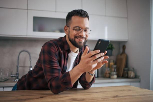 istock A smiling man is sitting in his modern kitchen and using a smartphone. 2072695315