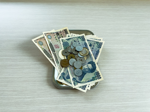 Banknotes and yen coins of various denominations are placed in a change tray on a wooden floor.