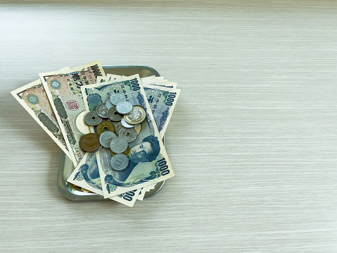 Banknotes and yen coins of various denominations are placed in a change tray on a wooden floor. Copy Space Background
