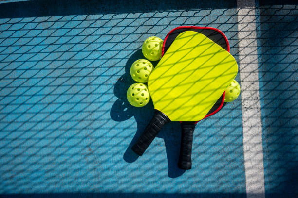 피클볼 패들과 공은 그물 그림자가 있는 피클볼 코트에 있습니다. - paddle ball racket ball table tennis racket 뉴스 사진 이미지