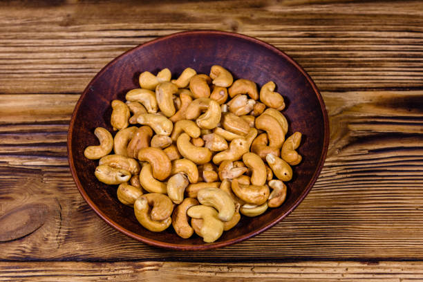 Ceramic plate with roasted cashew nuts on wooden table