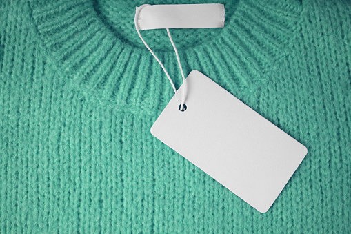 Blank clothing tag and inner label on neck of green knitted sweater background. Mockup, template with empty rectangular card for price or text. Shopping, sale, discount, black friday, fashion