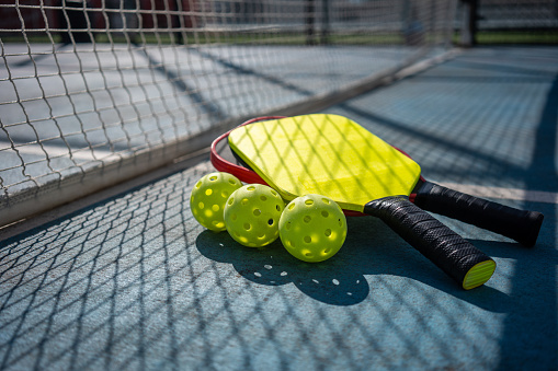 Pickleball Paddles and Balls are on Pickleball Court low angle point of view with net shadow