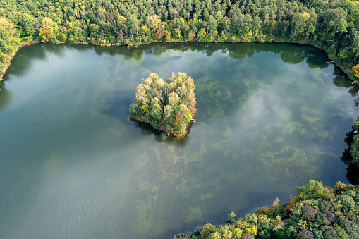 Aerial view of a small island on a green lake surrounded by forests in summer.