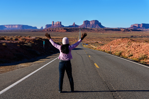 A tourist woman enjoys view of Monument valley at sunrise from the highway. Utah, USA