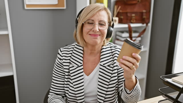 Smiling blonde woman wearing headphones holding coffee in modern office