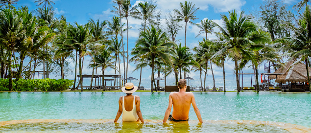 A man and a woman are lounging in a pool with palm trees all around them, enjoying the water and the beautiful sky above. They are relaxing in a tropical paradise