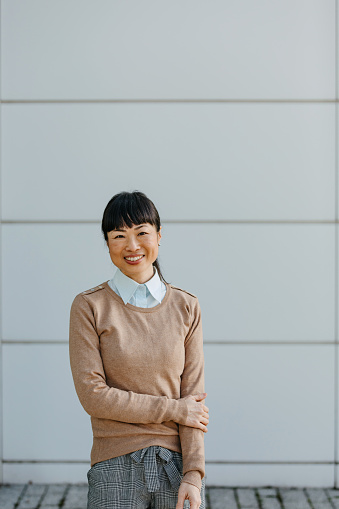 The mature Chinese businesswoman, captured in a portrait before a business edifice, personifies visionary leadership, her demeanor reflecting the wisdom, resilience, and foresight that have propelled her to the forefront of her industry