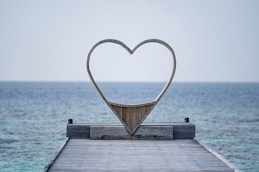 Wooden heart shaped chair looking through the sea  for couple, ocean background.