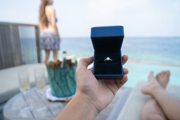 Hand holding a box with engagement ring with ocean view background.