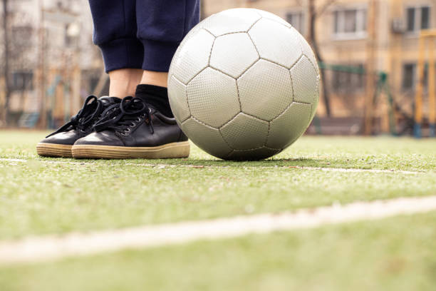 weibliche beine auf einem fußballfeld und ein grauer fußball in der ukraine, fußball spielen im hof - soccer field soccer single line field stock-fotos und bilder