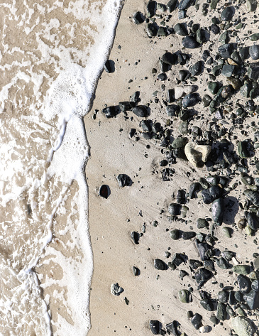 The waters of the Caribbean Sea flow up the sand towards the stones on the beach deposited by waves.