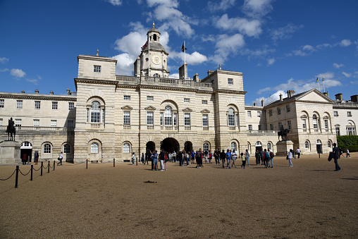 Horse Guards is a historic building in the City of Westminster, London, between Whitehall and Horse Guards Parade. It was built in the mid-18th century. The image shows the building exterior with several tourists, captured during summer season.