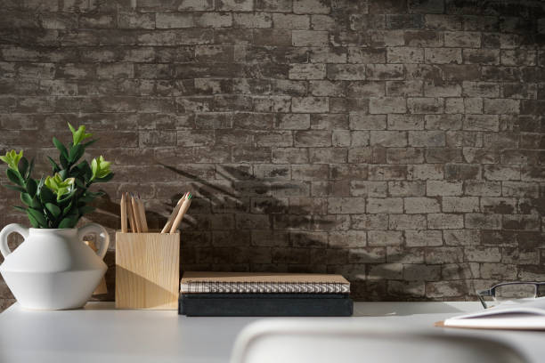 istock Creative workspace with blank poster frame, coffee cup, books and flower pot on white table with brick wall. 2072924735