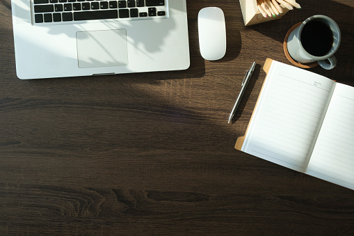 Top view of blank notepad, pen, cup of coffee, headphone and keyboard on woodden desk.