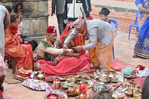 Kirtipur, Nepal - February 12, 2024 - A Newari Wedding starts with the ritual of, the groom side sending twelve areca nut in a huge silver bowl along with fruits, sweets, gold jewelry, clothes and other cosmetic accessories for the bride which are decorated and displayed in trays in an eye-catching way. The groom and the groom’s mother is absent in this ceremony whereas the bride’s mother starts the ceremony by worshipping lord Ganesh, lord of fire(Agni devta) and other god and goddesses. This ritual is usually performed four days before the wedding on the same day as the bride side’s reception party.
